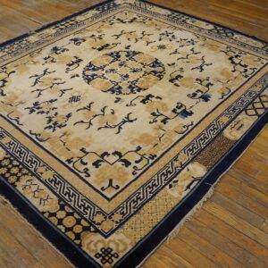 A traditional cream rug with navy blue and gold floral and geometric patterns lies on wide wooden floorboards.