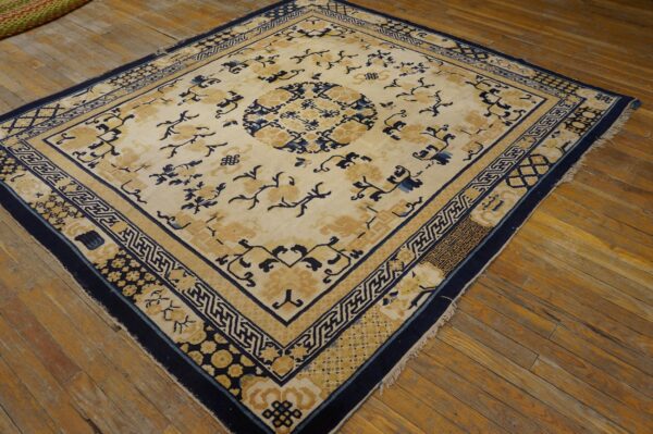 A traditional cream rug with navy blue and gold floral and geometric patterns lies on wide wooden floorboards.