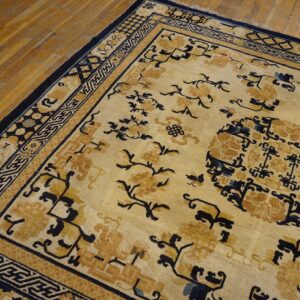 Cream and gold rug featuring dark blue floral patterns and geometric borders rests on aged wood planks.