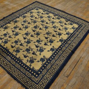 A square pale yellow rug featuring repeating blue florals and geometric borders rests on rustic wood planks.