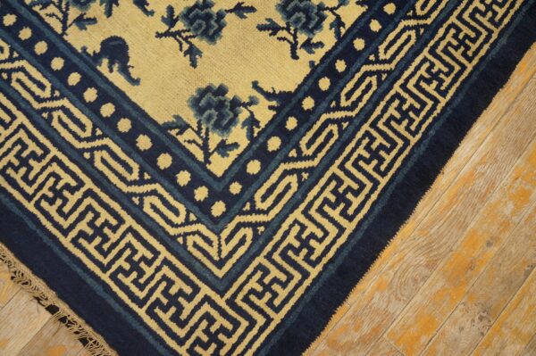 Navy blue and pale yellow rug border with meander patterns and florals lies on distressed wood flooring.