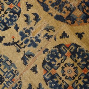 Worn tan rug with blue and coral geometric medallions and a visible vertical seam repair.