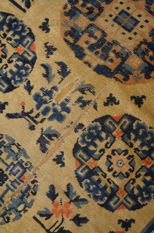Worn tan rug with blue and coral geometric medallions and a visible vertical seam repair.