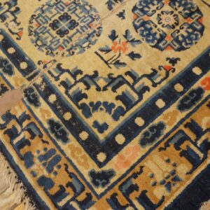 Corner view of a low-pile rug in tan and indigo with floral and geometric designs on light wood planks.