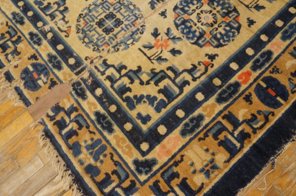 Corner view of a low-pile rug in tan and indigo with floral and geometric designs on light wood planks.