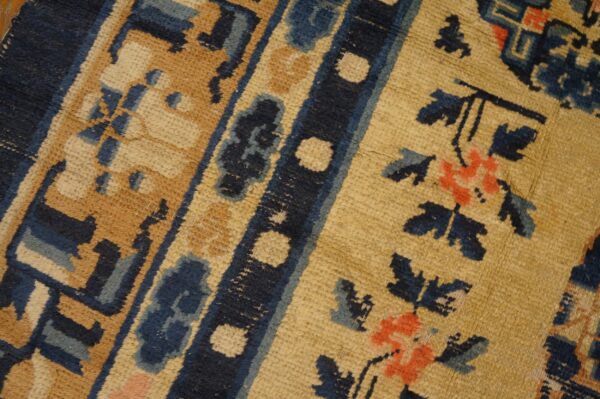 Low-pile rug detail featuring blue floral motifs, a golden field, and dark blue patterned borders.