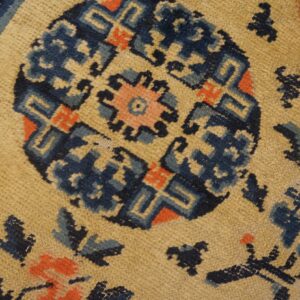 Low-pile rug detail showing a distressed tan field and geometric pattern in blue and coral.