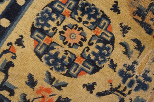 Low-pile rug detail showing a distressed tan field and geometric pattern in blue and coral.