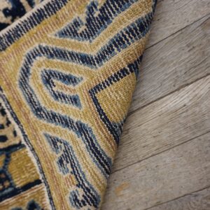 A patterned rug in gold, deep blue, and cream colors curves over gray wood planks.