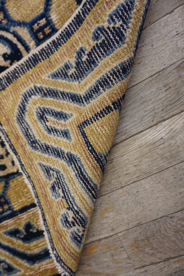A patterned rug in gold, deep blue, and cream colors curves over gray wood planks.