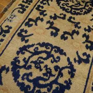 Textured tan rug featuring a repeating navy blue stylized pattern over hardwood planks.