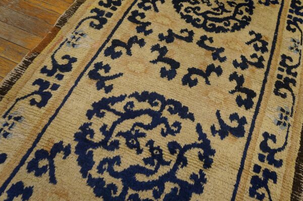 Textured tan rug featuring a repeating navy blue stylized pattern over hardwood planks.