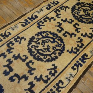 Tan runner rug with navy blue medallions and geometric borders resting on rustic wood planks.