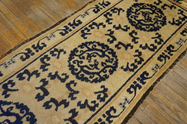 Tan runner rug with navy blue medallions and geometric borders resting on rustic wood planks.