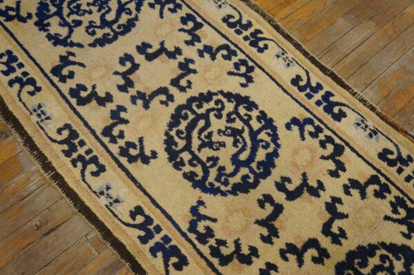 A long, textured beige runner with bold blue scrolling motifs rests on worn hardwood flooring.