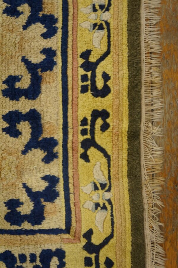 Textured rug detail showing yellow, navy, pink, and green borders with fringe on distressed wood flooring.