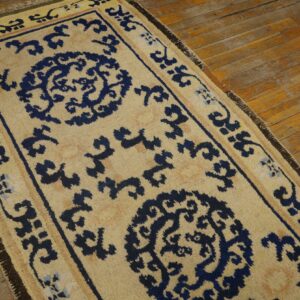 Beige runner rug with navy blue traditional medallions and scrollwork on worn wood plank flooring.
