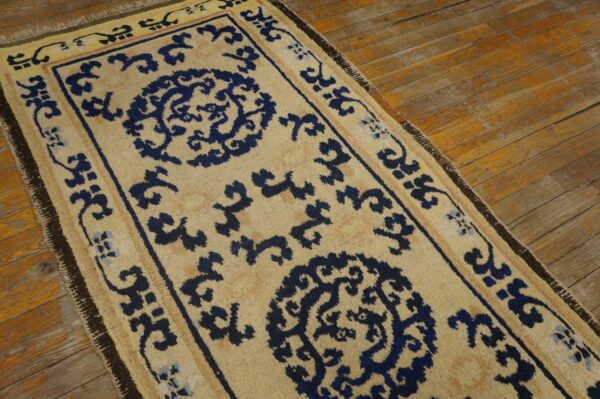 Beige runner rug with navy blue traditional medallions and scrollwork on worn wood plank flooring.