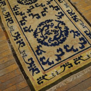 Tan and indigo medallion rug with yellow borders and fringe, displayed on rustic wood flooring.