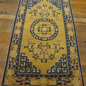 Yellow runner with indigo geometric borders and stylized floral motifs rests on worn wood planks.
