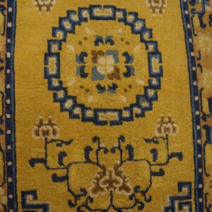Gold rug with navy blue and tan traditional patterns, including a medallion, resting on distressed wood flooring.