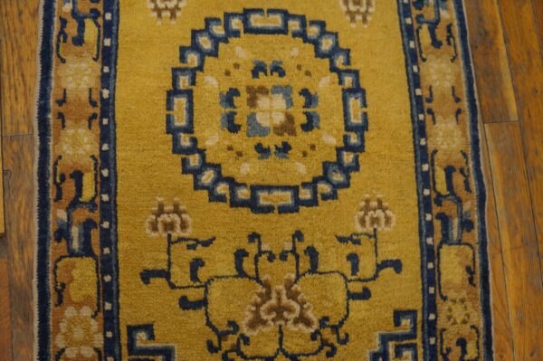 Gold rug with navy blue and tan traditional patterns, including a medallion, resting on distressed wood flooring.