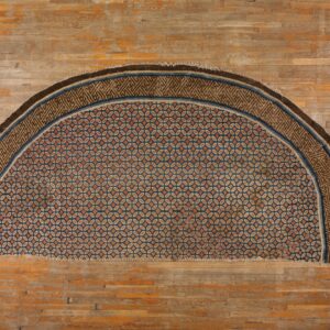 Half-circle rug patterned in orange, tan, and blue geometric medallions rests on distressed hardwood flooring.