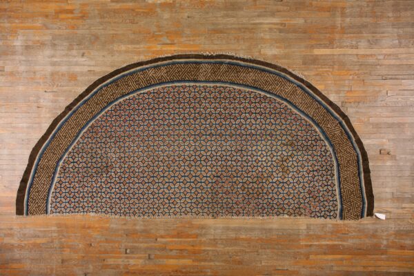 Half-circle rug patterned in orange, tan, and blue geometric medallions rests on distressed hardwood flooring.