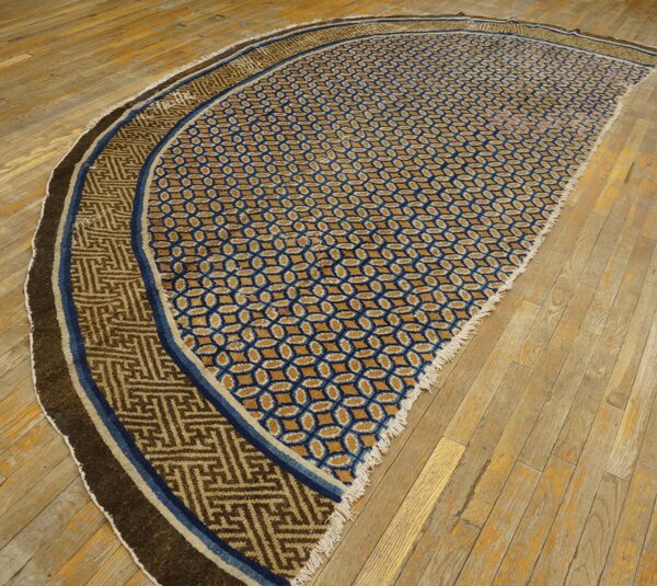 Curved rug featuring blue lattice and tan fret patterns, set upon worn plank wood flooring.