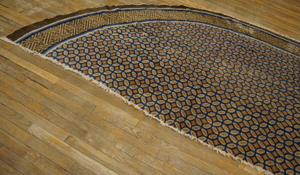 A semicircular blue and gold rug with geometric patterns and fringe rests on distressed wood floorboards.