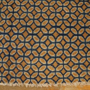 Textured rug with a geometric gold and navy lattice pattern, ending in white fringe on a wood floor.