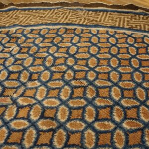 Brown and blue high-pile rug features an oval geometric pattern and a complex border on wood flooring.