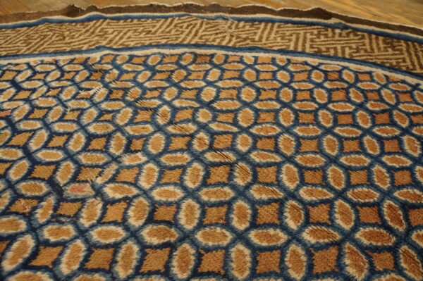 Brown and blue high-pile rug features an oval geometric pattern and a complex border on wood flooring.