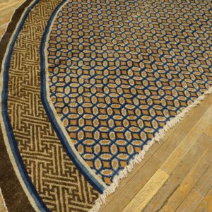 Curved blue and gold patterned rug section featuring a brown Greek key border on distressed wood flooring.