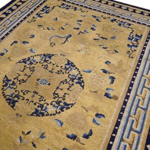 Tan and gold rug with a dark blue central motif and complex border featuring geometric fret patterns.