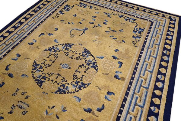 Tan and gold rug with a dark blue central motif and complex border featuring geometric fret patterns.