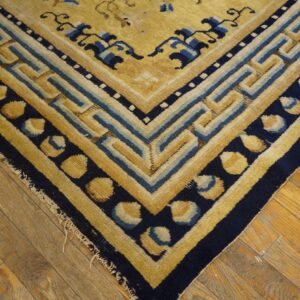Geometric gold and navy rug border featuring a fret pattern lies on worn wooden floors.