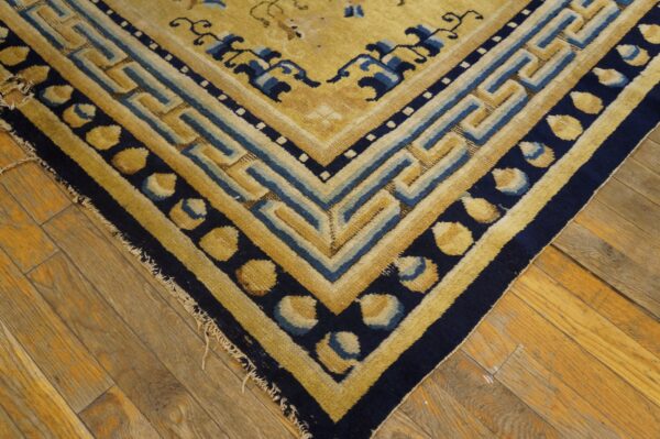 Geometric gold and navy rug border featuring a fret pattern lies on worn wooden floors.