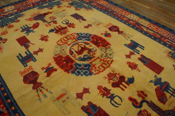 Angled view of a low-pile gold rug with scattered red and navy pictorial motifs on wooden planks.