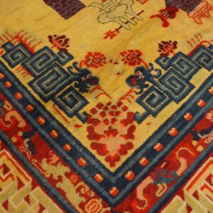 Textured rug corner displaying yellow field, deep blue meander pattern, and thick red geometric borders.