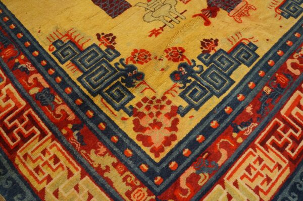 Textured rug corner displaying yellow field, deep blue meander pattern, and thick red geometric borders.