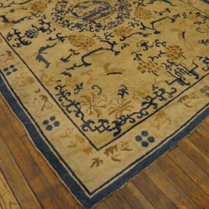 Tan rug with a dark blue border and stylized floral patterns lying on warm, rustic wood plank flooring.
