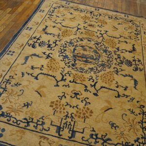 Tan and navy patterned rug featuring floral and geometric motifs displayed on worn hardwood planks.