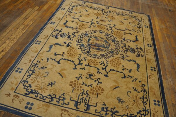Tan and navy patterned rug featuring floral and geometric motifs displayed on worn hardwood planks.