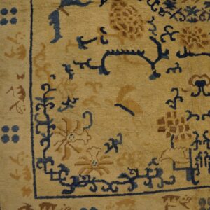 Beige rug with indigo and gold scrolling floral patterns rests on dark brown wood flooring.