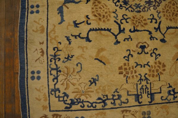 Beige rug with indigo and gold scrolling floral patterns rests on dark brown wood flooring.