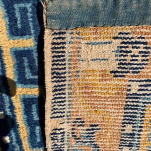 Detailed view of a high-pile blue and gold pattern adjacent to a multi-colored flatweave section stitched with blue twill fabric.