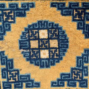 Close-up of a rug pattern featuring golden yellow and deep blue geometric step-fret and medallion motifs.
