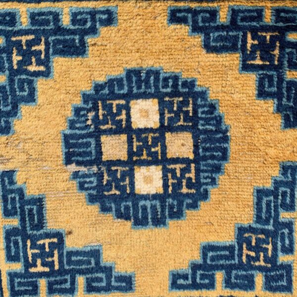 Close-up of a rug pattern featuring golden yellow and deep blue geometric step-fret and medallion motifs.