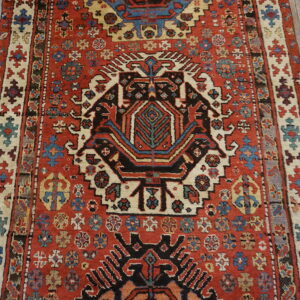 Rust red geometric rug with a black and cream central medallion rests on rustic wooden floors.
